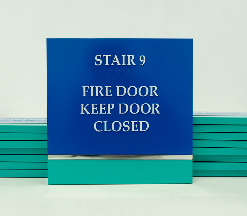 Blue and teal room sign in front of a stack of signs