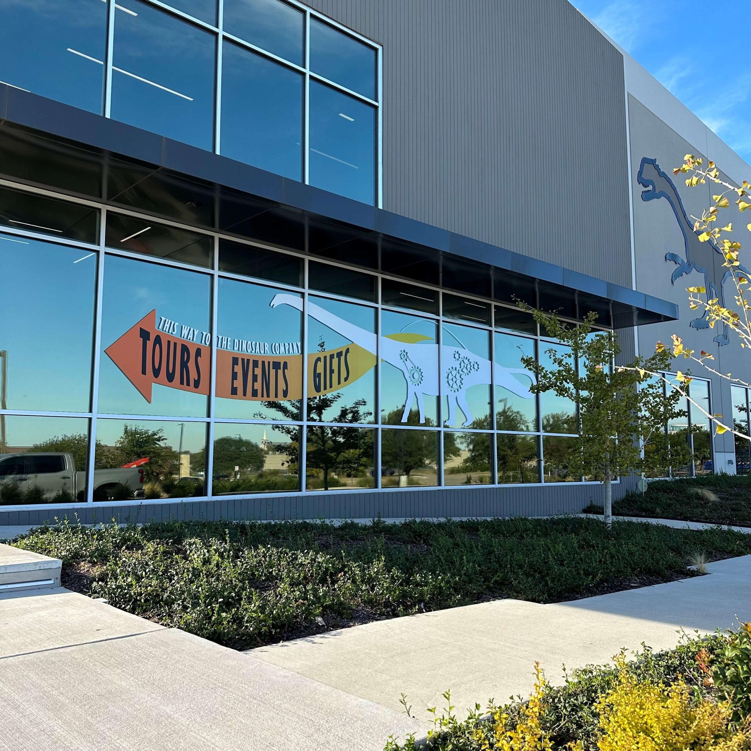 An outdoor vinyl window graphic that reads "THIS WAY TO THE DINOSAUR COMPANY TOURS EVENTS GIFTS" with a vinyl cut out of a Brachiosaurus.