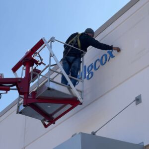 A man on a cherry picker installing the logo for a business