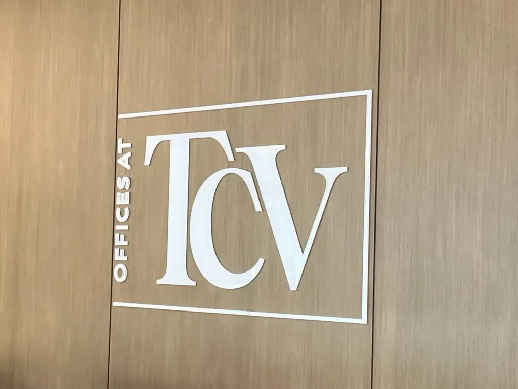 Dimensional TCV logo lettering on a wood panel wall in a corporate office reception